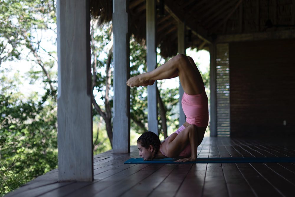 Woman practicing an advanced yoga pose on an open-air deck surrounded by nature at a yoga retreat in Nicaragua