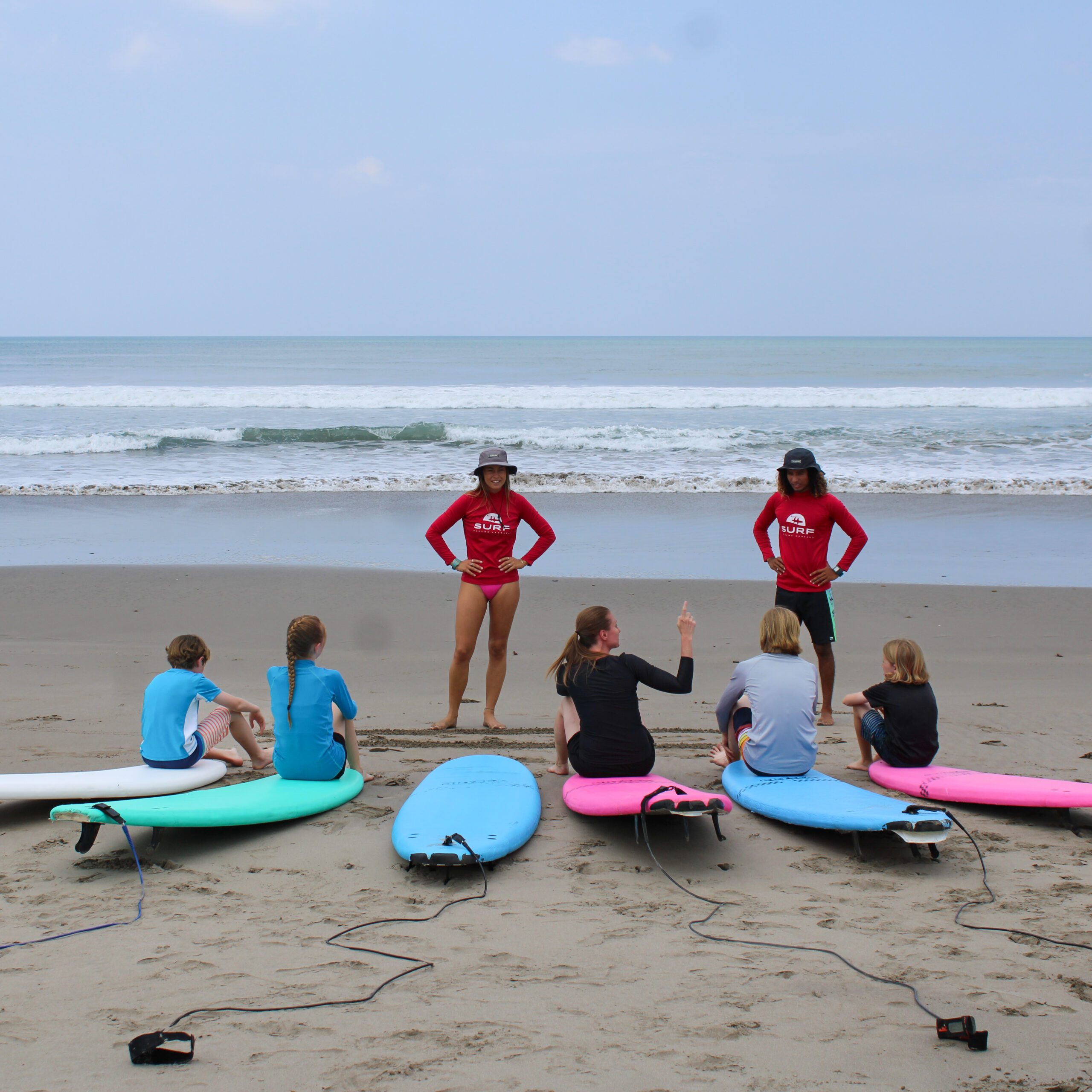 http://A%20group%20of%20children%20sits%20on%20the%20sand%20with%20surfboards%20while%20two%20instructors%20in%20red%20shirts%20and%20hats%20stand%20in%20front%20of%20them%20on%20a%20beach,%20with%20waves%20and%20a%20cloudy%20sky%20in%20the%20background.