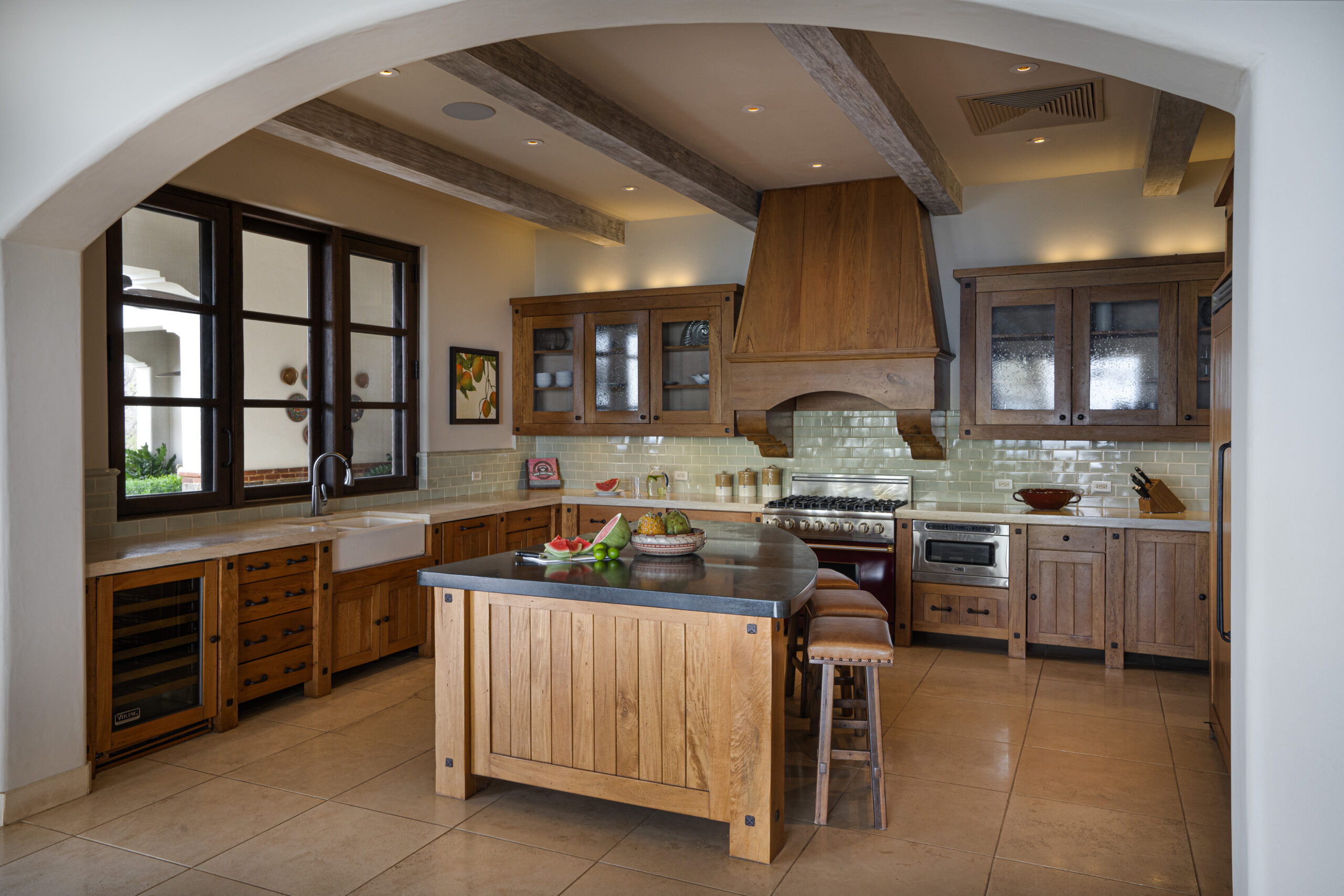 http://A%20spacious%20kitchen%20in%20Villa%20Escondida%20features%20wooden%20cabinets,%20a%20central%20island%20with%20stools,%20stainless%20steel%20appliances,%20a%20farmhouse%20sink,%20and%20a%20large%20window.%20Light%20tile%20flooring%20and%20exposed%20beams%20add%20warmth%20to%20this%20co-owned%20luxury%20home.