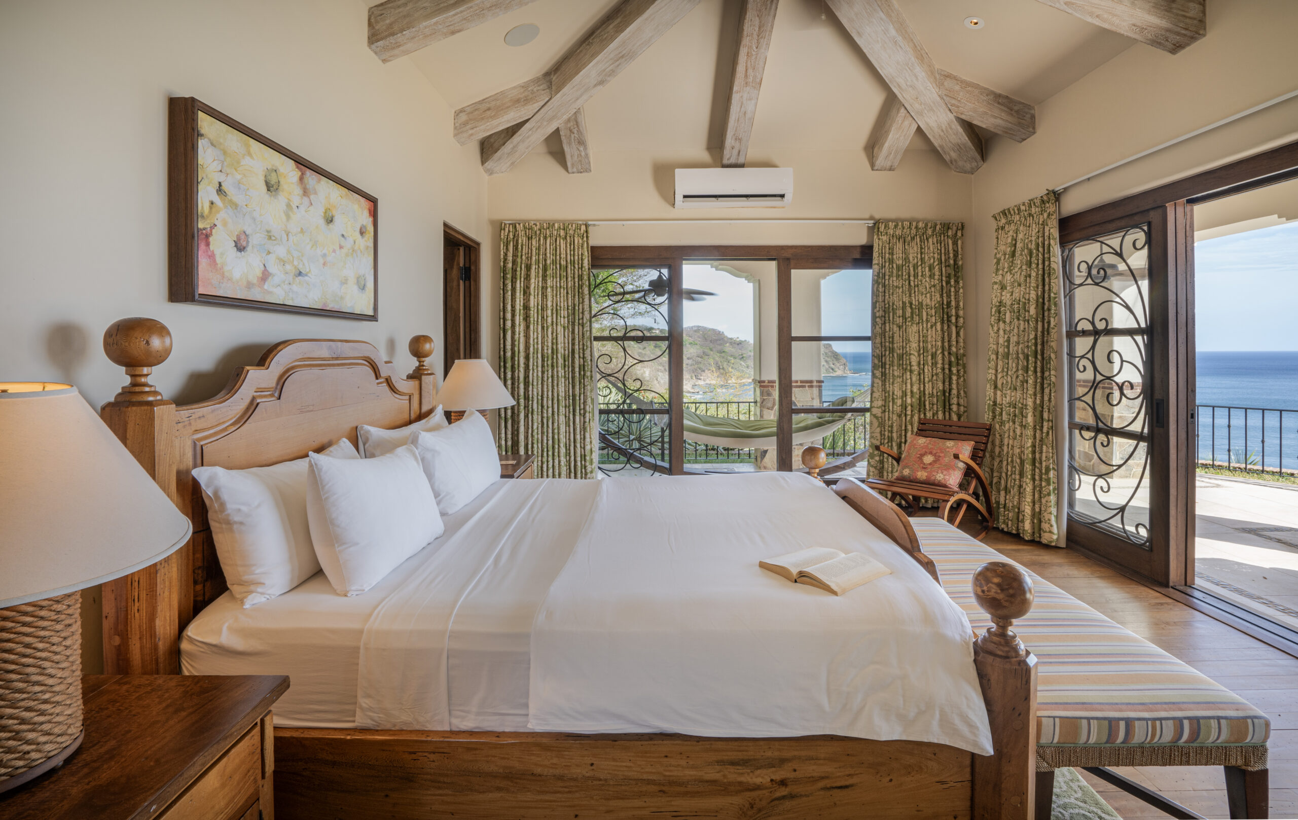 http://A%20cozy%20bedroom%20in%20Villa%20Escondida%20features%20a%20wooden%20bed,%20white%20bedding,%20and%20a%20book%20on%20the%20bed.%20Large%20windows%20open%20to%20a%20balcony%20with%20ocean%20views—perfect%20for%20relaxing%20in%20your%20co-owned%20luxury%20home%20surrounded%20by%20exposed%20wood%20beams,%20floral%20art,%20and%20natural%20light.