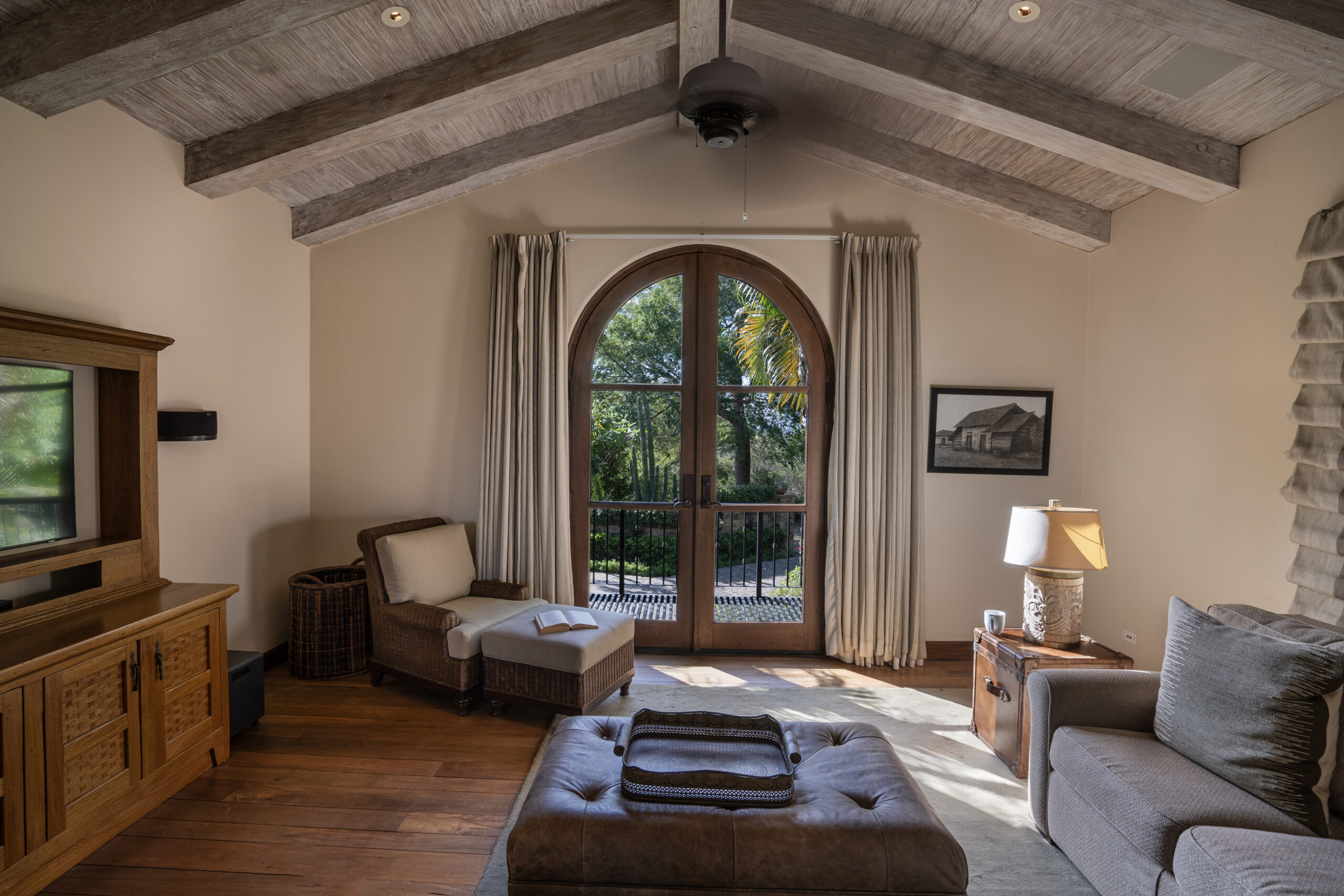http://A%20cozy%20living%20room%20in%20Villa%20Escondida%20features%20a%20wood-beamed%20vaulted%20ceiling,%20large%20arched%20window%20with%20curtains,%20armchair,%20sofa,%20ottoman,%20side%20table%20with%20lamp,%20and%20wooden%20TV%20stand%20on%20hardwood%20floors%20in%20this%20co-owned%20luxury%20home.