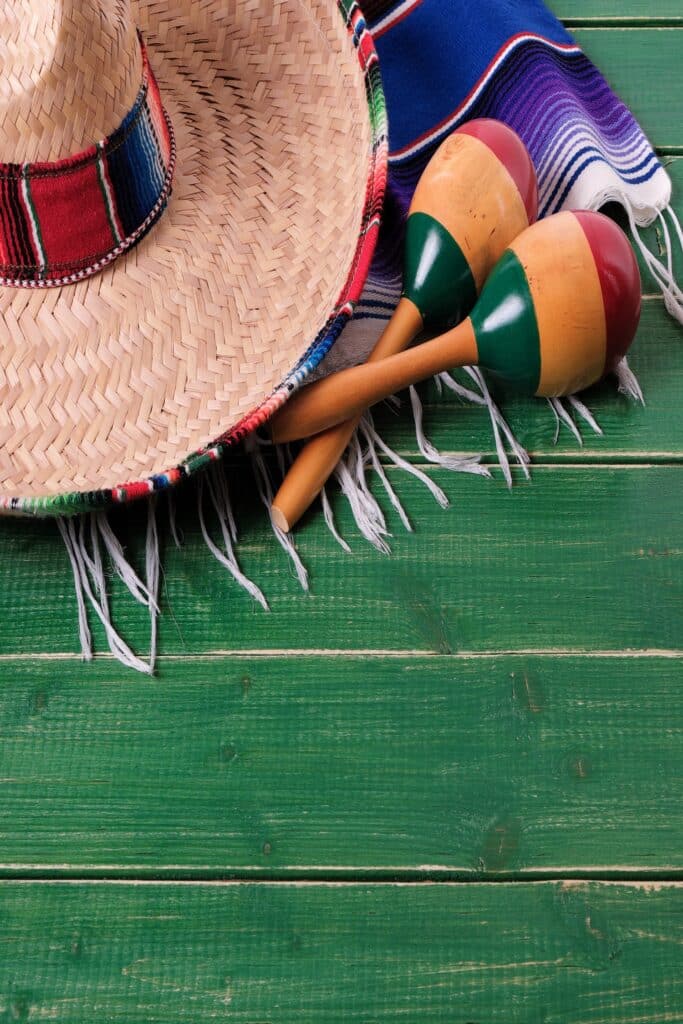 A woven sombrero hat, two wooden maracas, and a colorful striped blanket are arranged on a green wooden table—evoking the vibrant spirit of under-the-radar destinations perfect for your next luxury travel adventure.